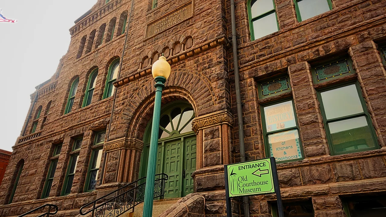 The arched entrance of the Old Minnehaha County Courthouse, its quartzite masonry framed by weathered copper doors.