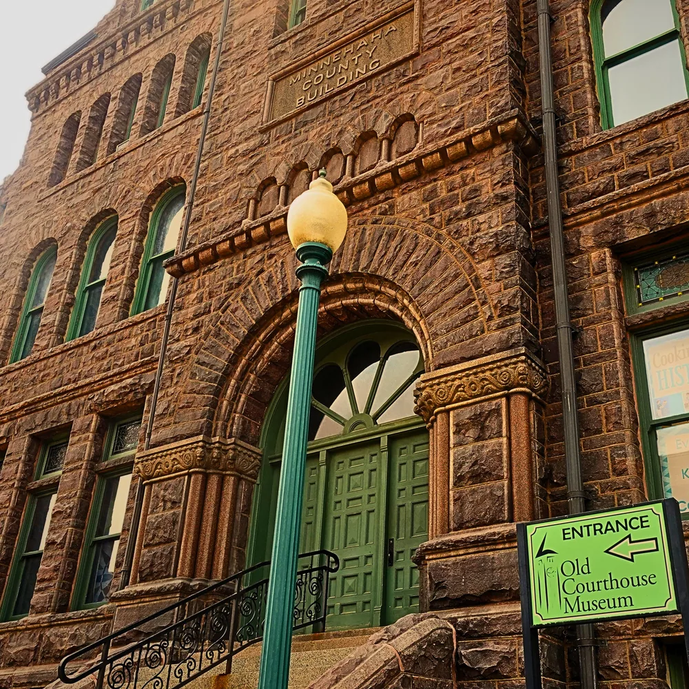 The arched entrance of the Old Minnehaha County Courthouse, its quartzite masonry framed by weathered copper doors.